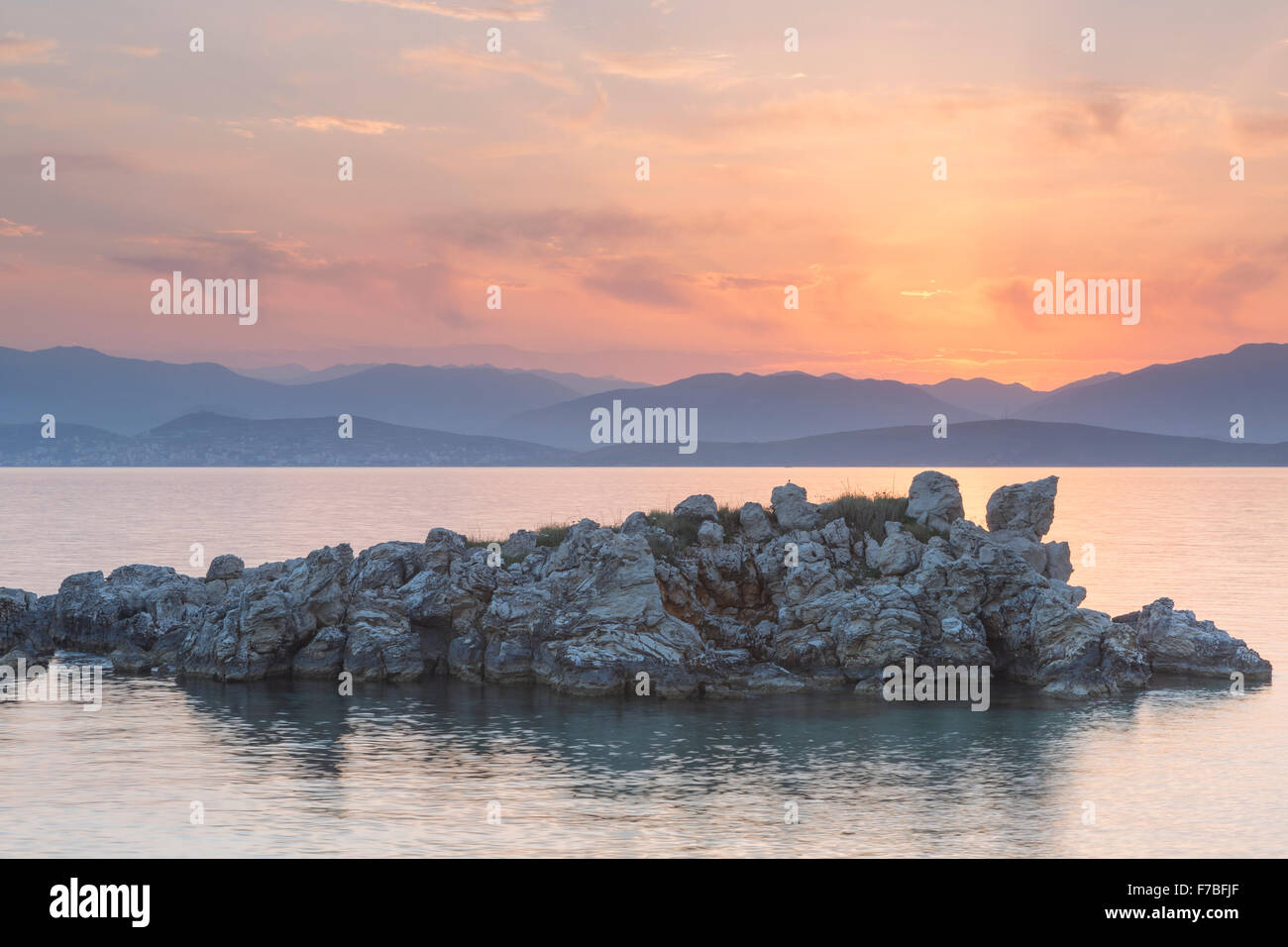 Felsen ragen aus dem Ionischen Meer in der Straße von Korfu in der Nähe von Kassiopi, Corfu. Die Sonne geht über Albanien. Stockfoto