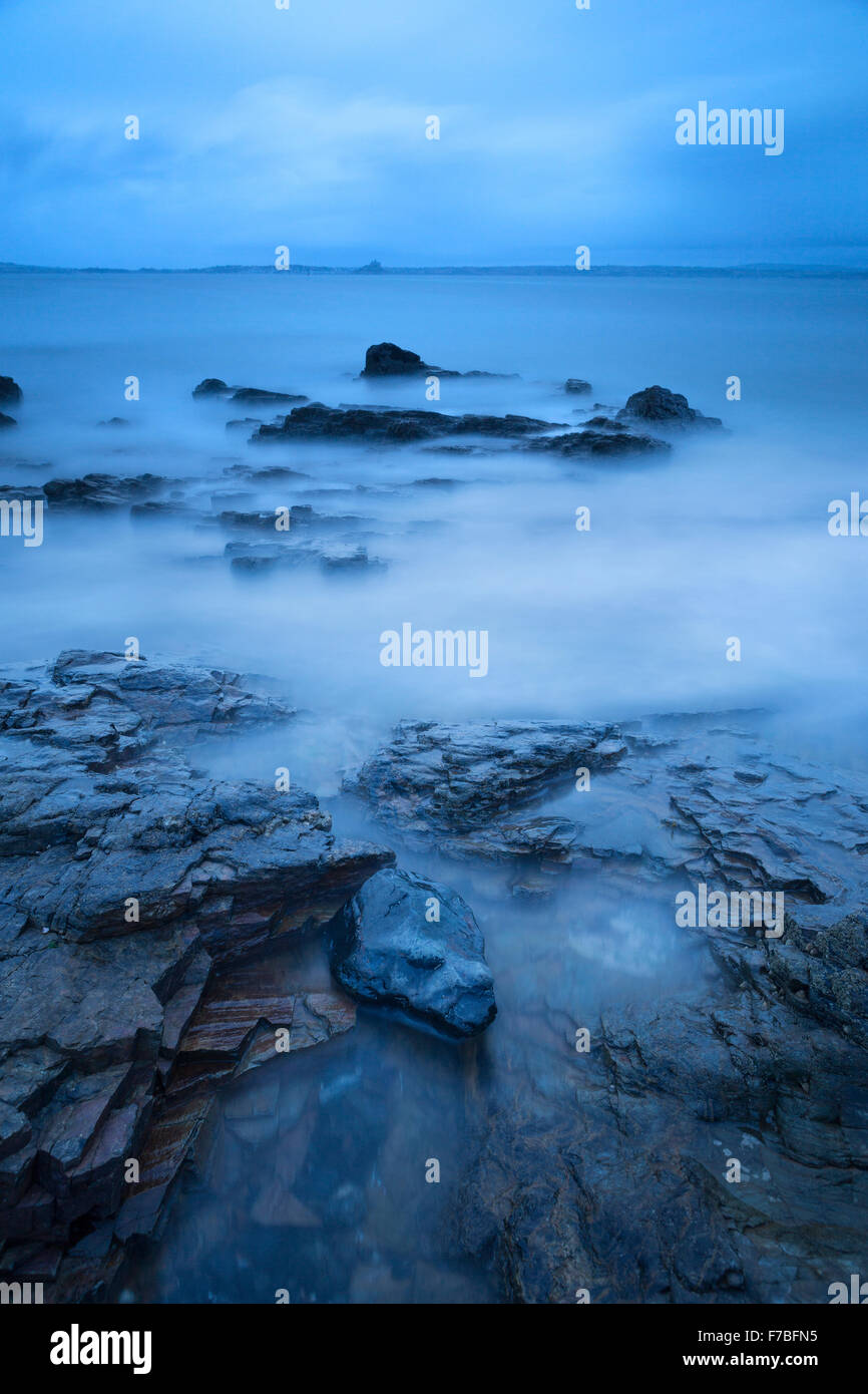 Wellen Waschen über den Felsen kleben aus blaues Meer in Mousehole Cornwall. Mont Saint Michel zu sehen in der Ferne Stockfoto