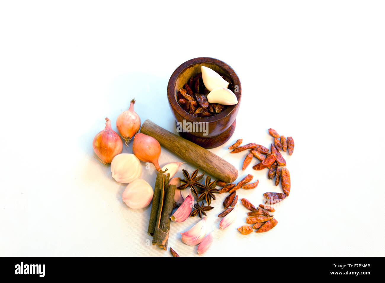 Stößel und Mörser und Gewürze (trockene Chilis, Knoblauch, Zwiebeln, Anisered, Zimt) auf weißem Hintergrund Stockfoto