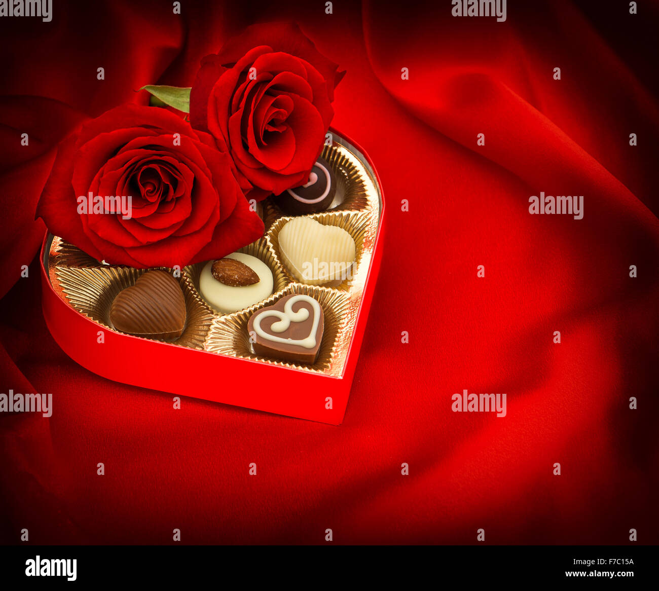 Rote Rosen und Pralinen in goldenen herzförmige Geschenkbox auf satin Hintergrund Stockfoto