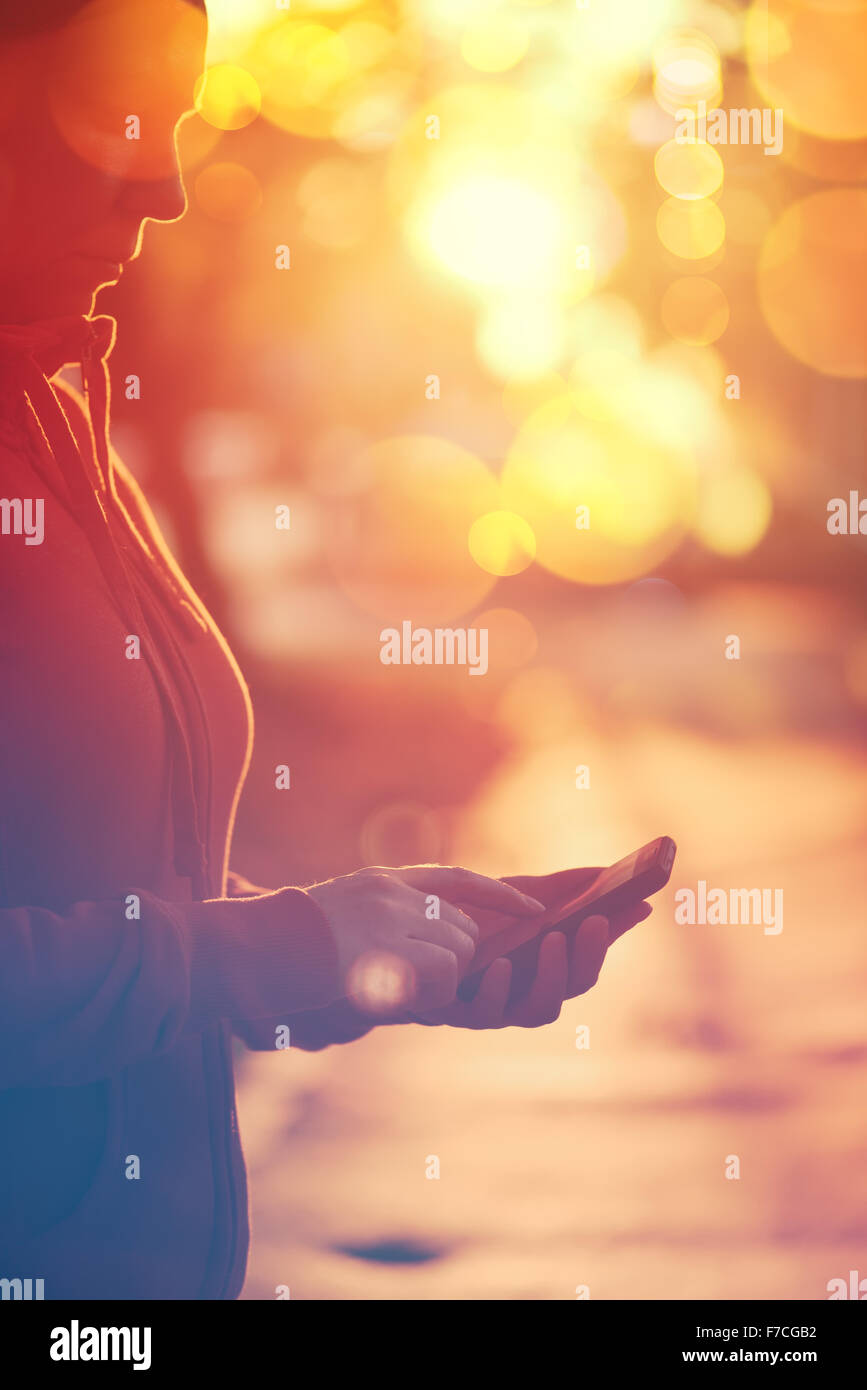 Retro-getönten Bild Frau mit mobile Smartphone im freien Einstellung, späten Nachmittag, selektiven Fokus mit Bokeh leichte Zeitmessung Stockfoto