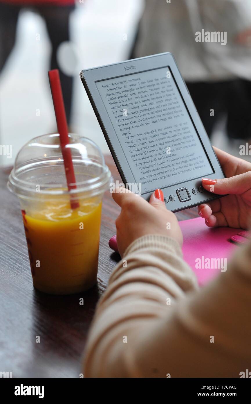 Eine Mädchen liest ein Amazon Kindle in einem Café mit einem orange Smoothie. Stockfoto