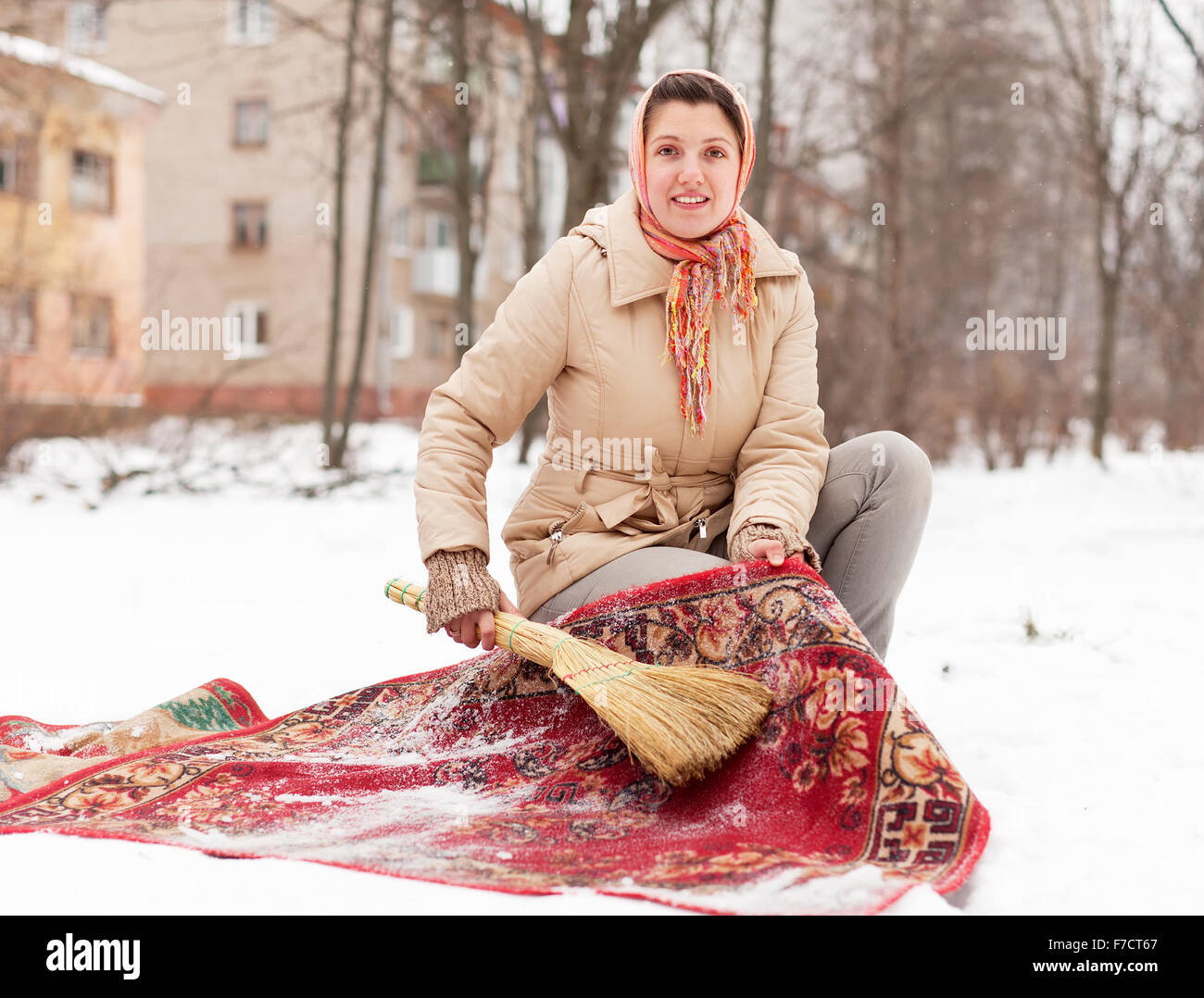 Junge Frau reinigt roten Teppich mit Schnee im Wintertag im freien Stockfoto