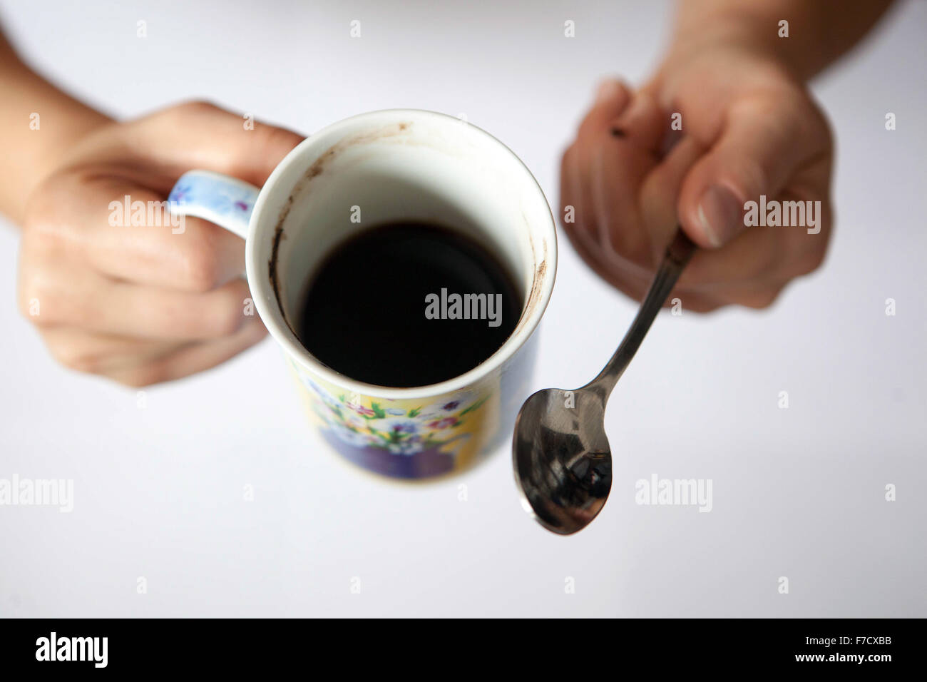 Eine Tasse schwarzen Morgenkaffee in weiblichen Händen. Kaffeetasse vom Löffel Stockfoto