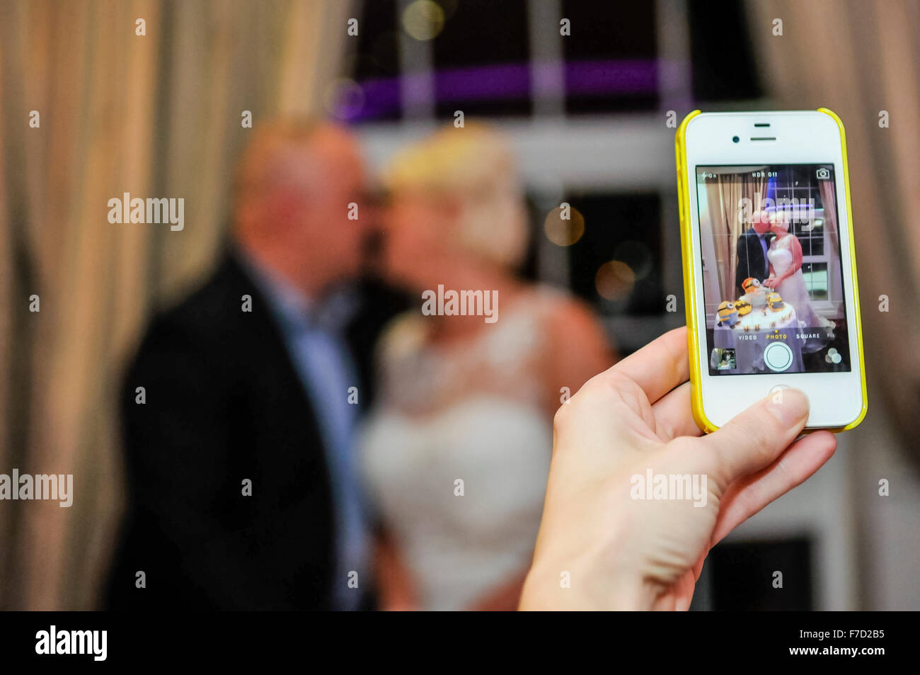 Ein Gast auf einer Hochzeit fotografiert der Braut und des Bräutigams teilen einen Kuss. Stockfoto