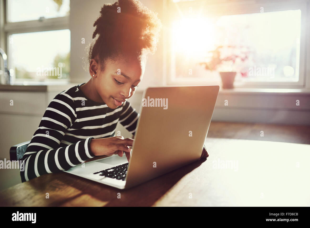 Ethnische Mädchen mit niedlichen Afro Frisur sitzt zu Hause verwenden einen Laptop-Computer ihre Klasse Arbeit zu tun und Surfen im Internet, bri Stockfoto