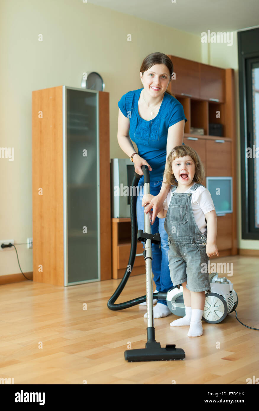 Frau lehrt Mädchen, den Staubsauger zu Hause zu verwenden Stockfoto