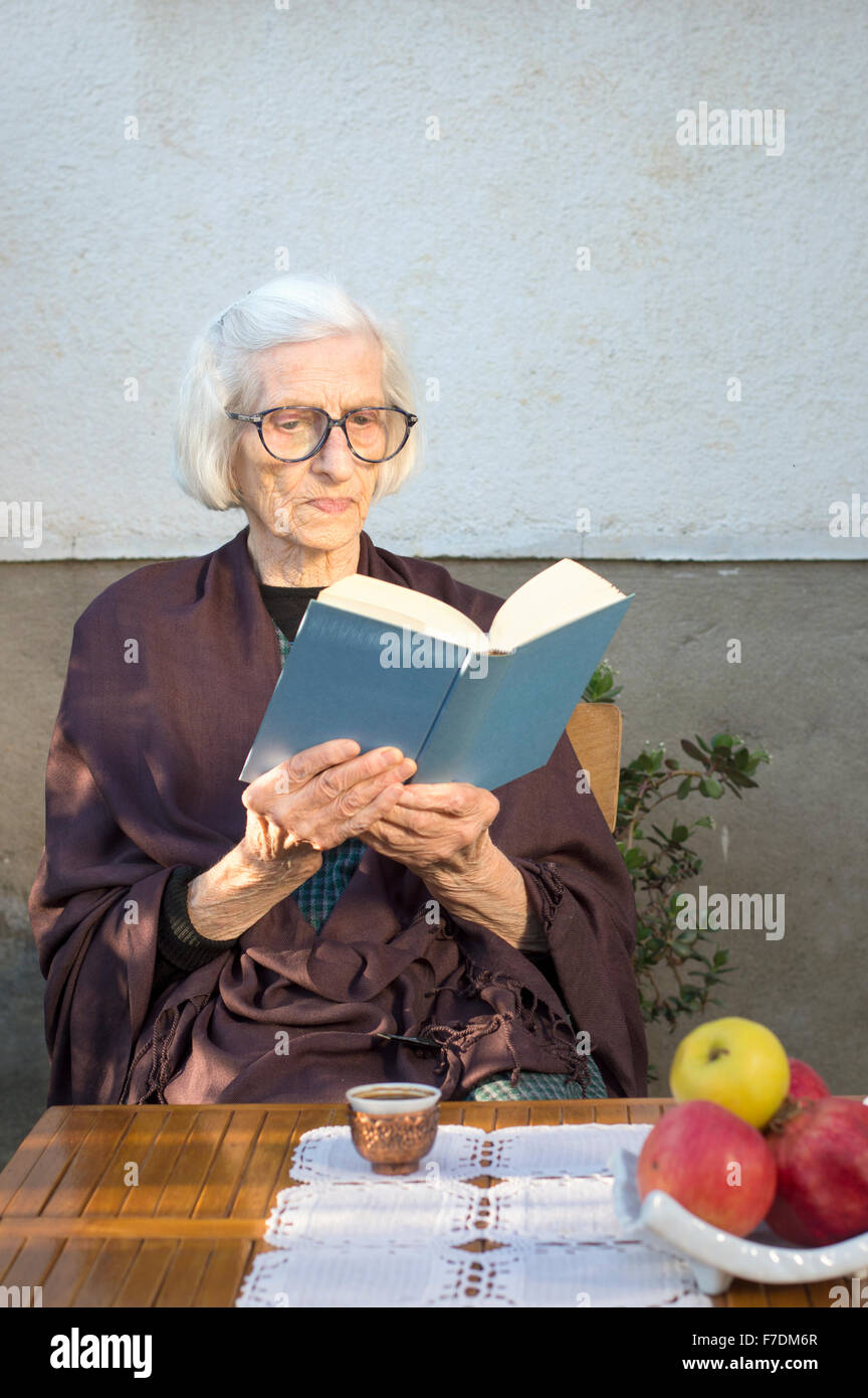 Alte Frau ein Buch lesen und Tasse Kaffee im Garten Stockfoto
