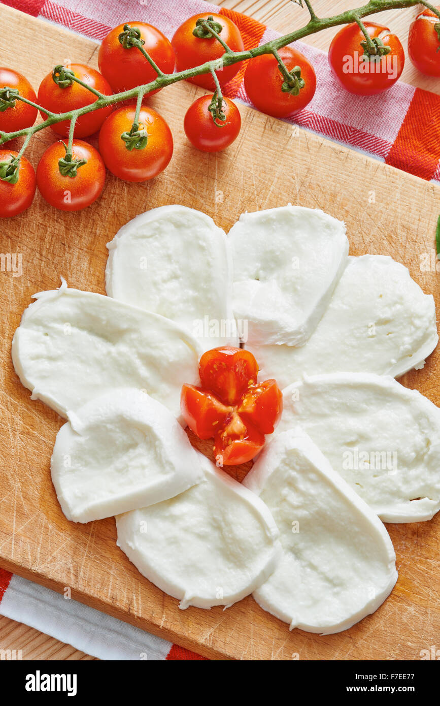 In Scheiben geschnittenen Mozzarella auf Schneidebrett umgeben von Tomaten und Basilikum auf einem Holztisch Stockfoto