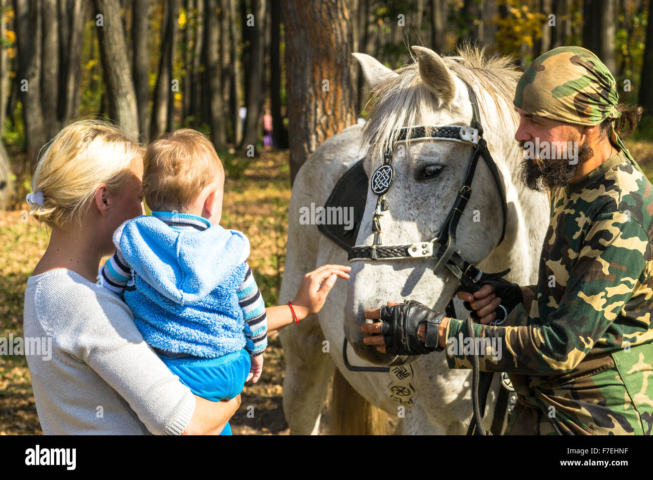 23/09 - Mann in militärische Tarnung Strichen ein weißes Pferd als Frau und junge Baby schauen Sie sich den Ausdruck der Zuneigung in Ufa Ru Stockfoto