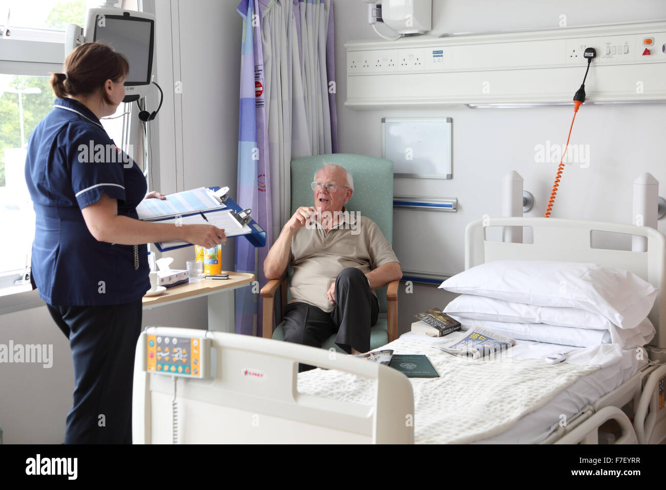 Eine Krankenschwester spricht mit einem älteren Patienten in einer modernen Krankenhausabteilung in Großbritannien. Broomfield Hospital, Essex. (Identifizierung von Namen und medizinischen Daten entfernt) Stockfoto
