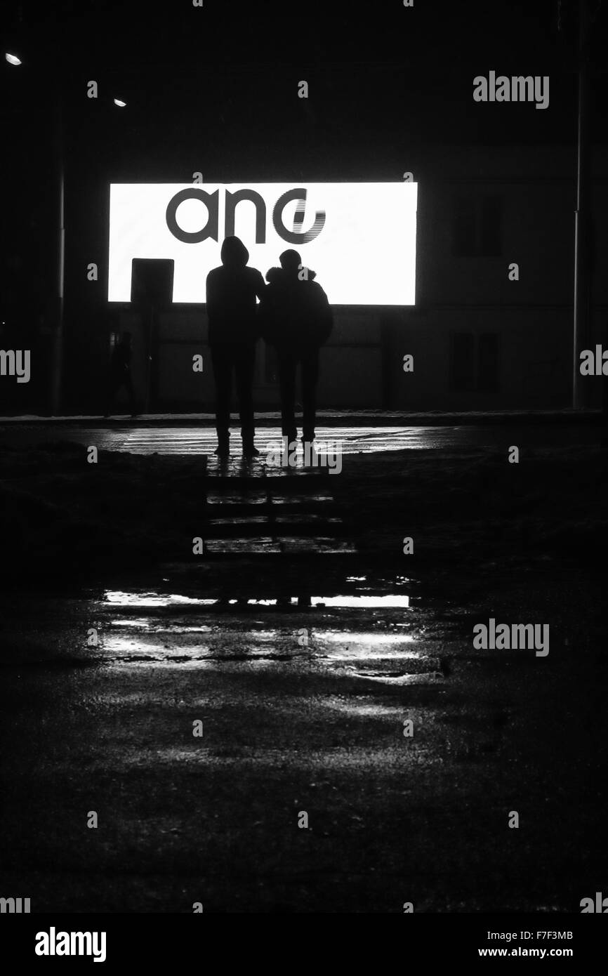 Zwei Fußgänger warten, um einen Regen durchnässt Straße vor einem großen LED Werbung Fernsehrat zu überqueren.  Dieses Foto war capt Stockfoto