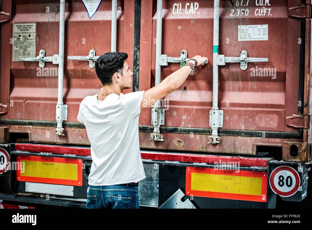 Taille bis Porträt des jungen lächelnd Mann neben LKW - entladen von Fracht aus Container Stockfoto