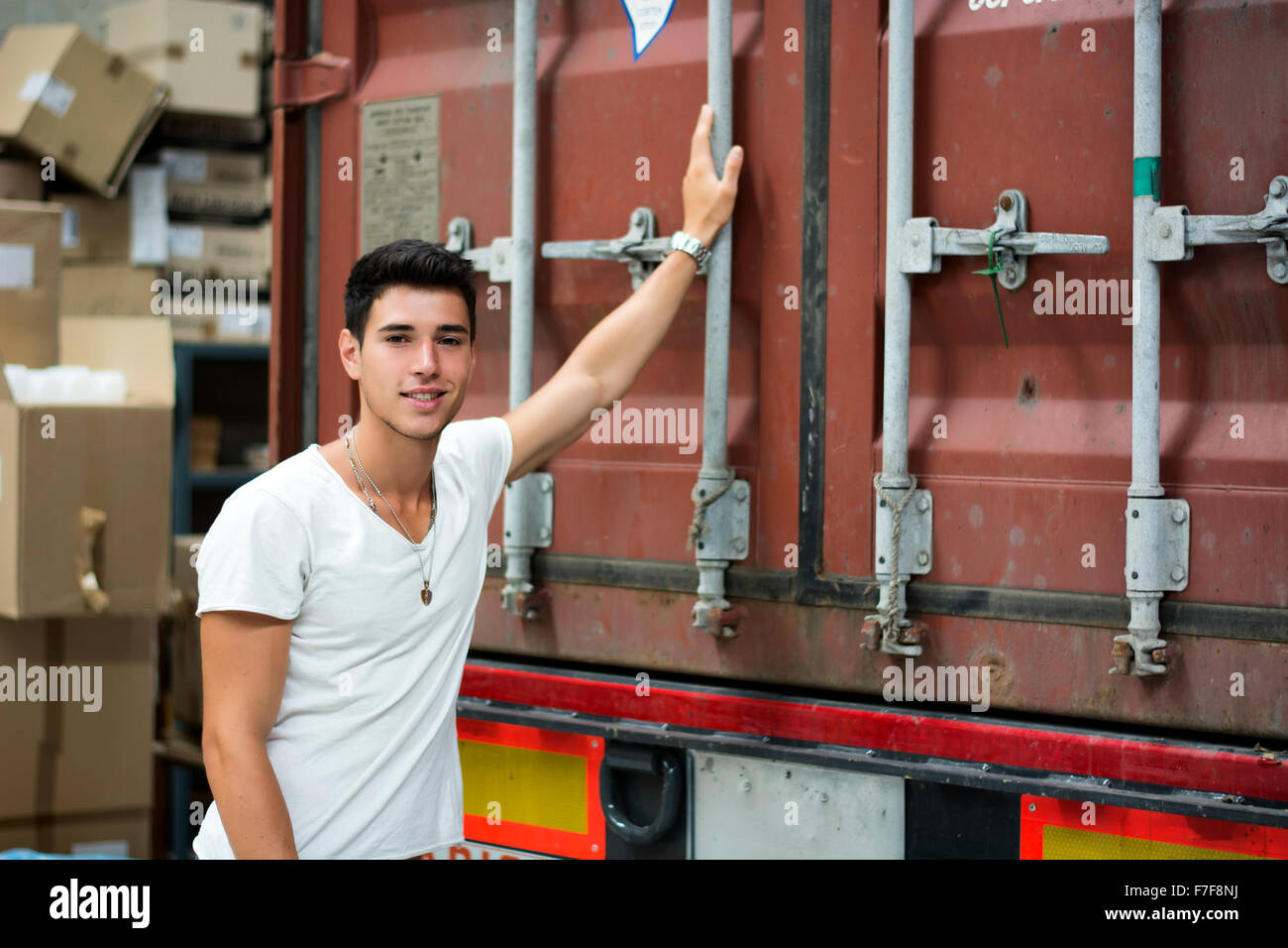 Taille bis Porträt des jungen lächelnd Mann neben LKW - entladen von Fracht aus Container Stockfoto