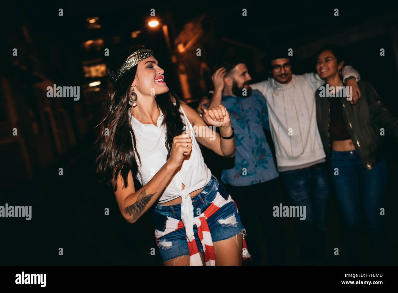 Porträt der hübschen jungen Frau tanzt mit ihren Freunden im Hintergrund. Glückliche junge weibliche genießen in einer Party mit Freunden. Stockfoto