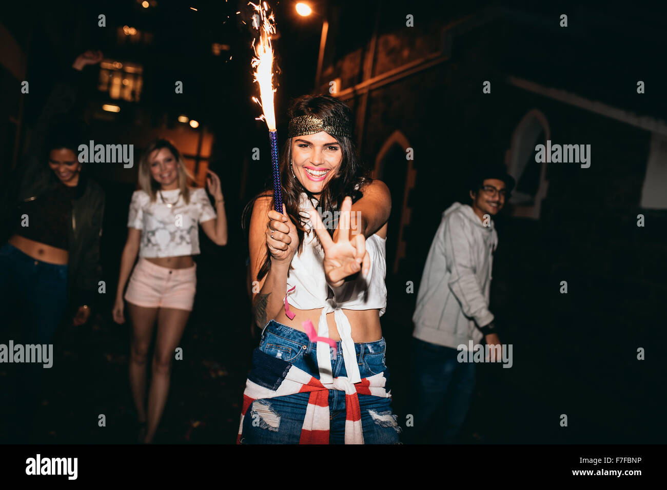 Porträt der fröhliche junge Frau hält eine Wunderkerze und zeigt Victory-Zeichen. Jugendliche feiern 4. Juli bei Nacht outd Stockfoto