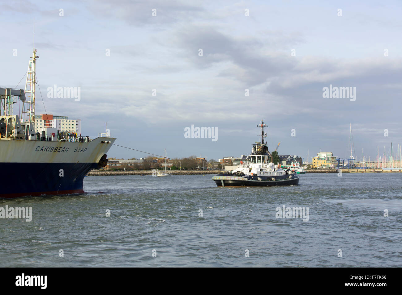 Arbeitsboot Schlepper Führung ein großes Containerschiff durch den schmalen Eingang des Hafens von Portsmouth. Stockfoto