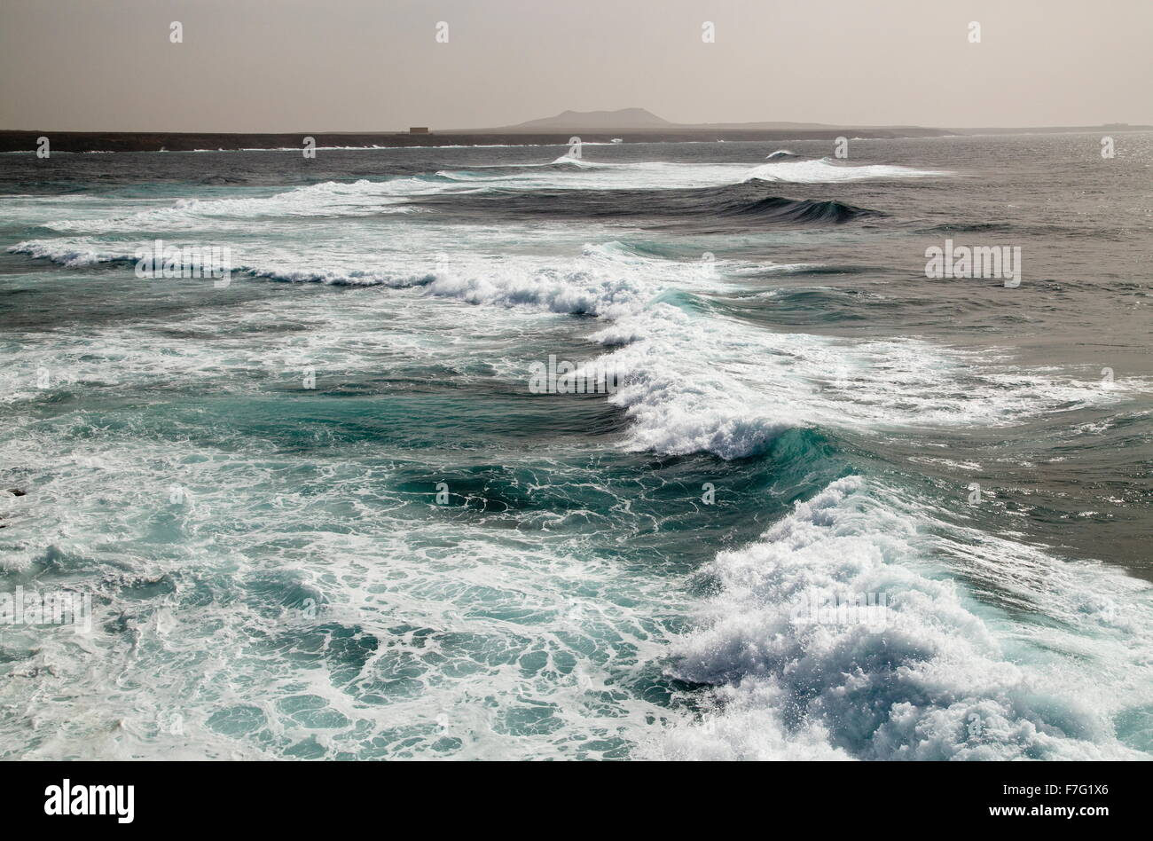 Strand mit Brandung am Playa de Janubio, mit Montana Roja und Entsalzungsanlage jenseits; Südwesten Lanzarotes. Stockfoto