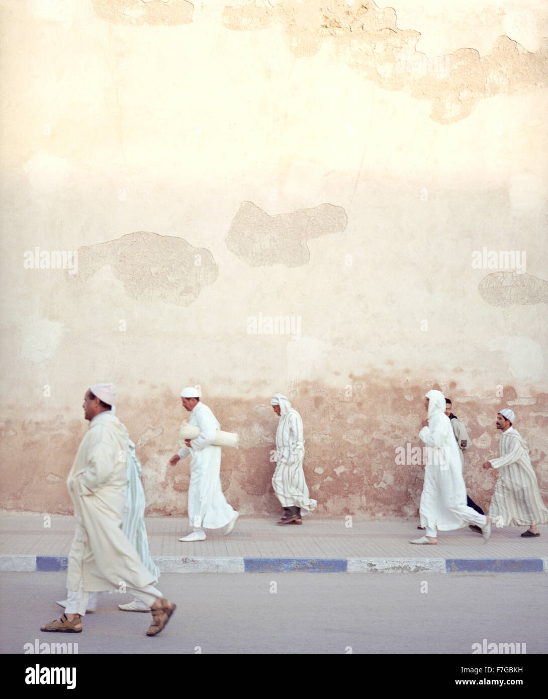 Marokkanische muslimische Männer gehen zügig vorbei an der Stadtmauer auf dem Weg zum Morgengebet. Essaouira, Marokko, Nordafrika. Stockfoto