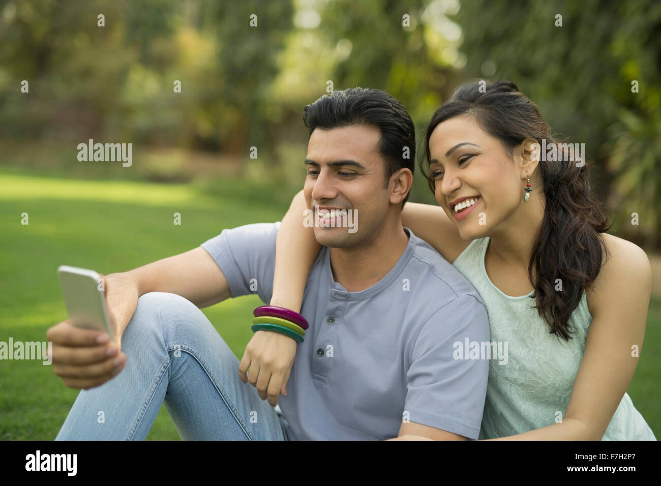 Mann und Frau sitzen auf dem Rasen Blick auf Handy Stockfoto