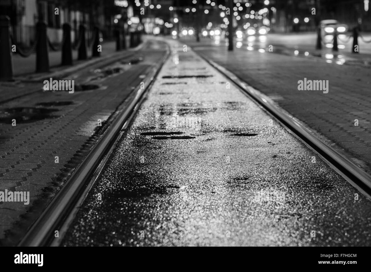 Nacht Blick auf nasse Straßenbahnschienen nach Regen. Verschwommene Ampel auf Hintergrund, schwarz / weiß-Ton Stockfoto