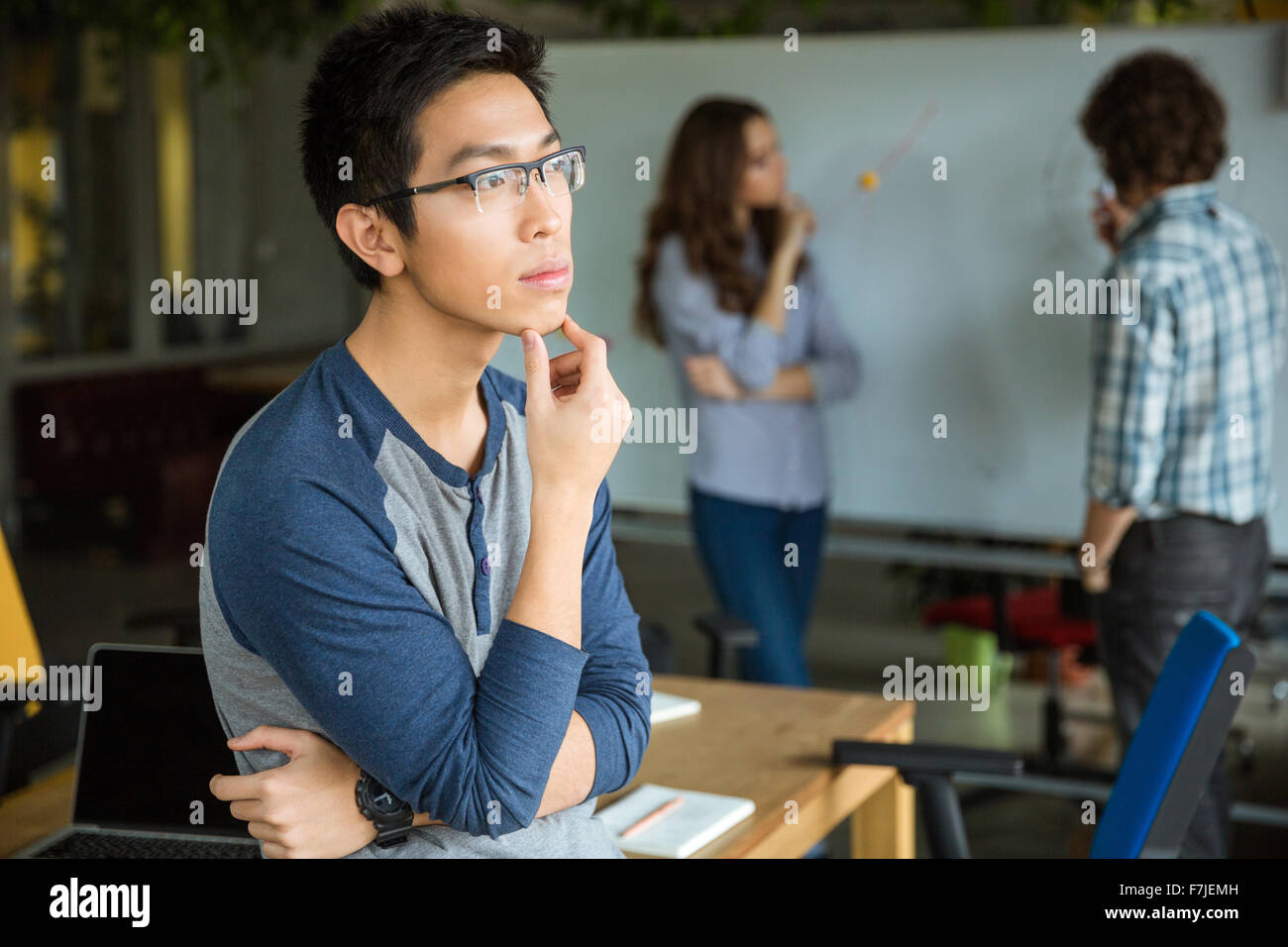 Nachdenklich konzentrierte hübscher junger asiatischer Mann in Gläsern denken und arbeiten mit Kollegen Stockfoto