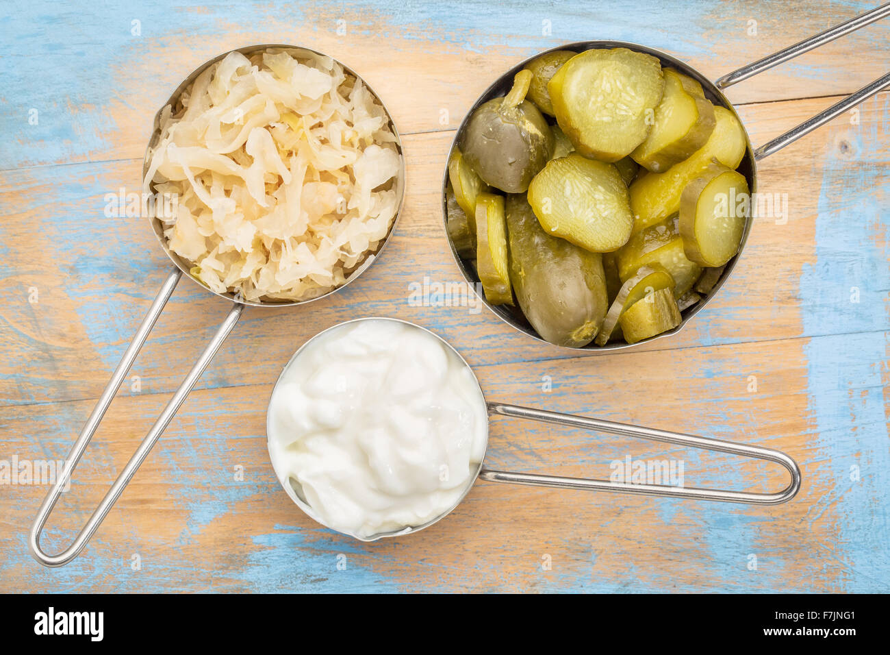 Sauerkraut, Gurken Essiggurken und Joghurt - fermentiert beliebte probiotische Lebensmittel - drei Messbecher gegen rustikale Holz Stockfoto