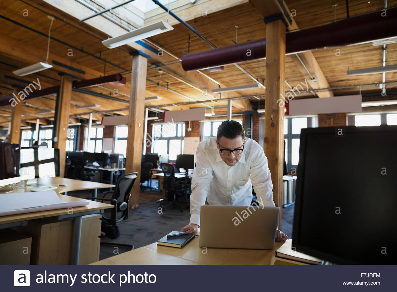 Geschäftsmann, beugte sich über Laptop im Großraumbüro Stockfoto