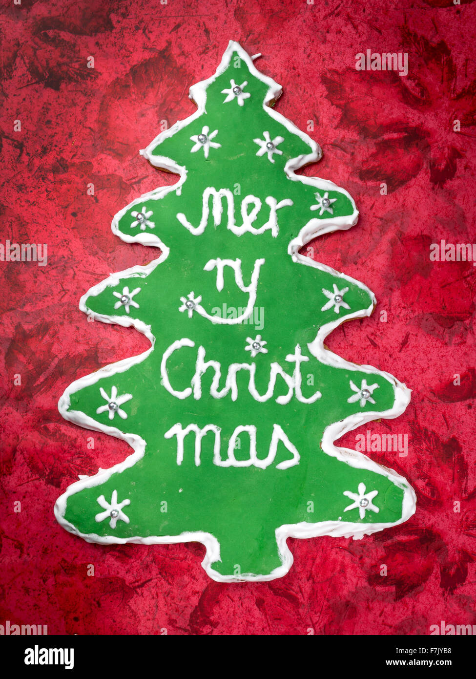 Weihnachtsbaum-wie Lebkuchen mit grüner Glasur und Frohe Weihnachten schreiben auf rotem Grund Stockfoto