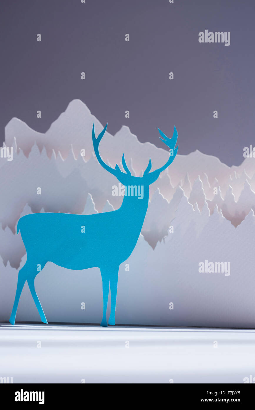 Handgeschöpftes Papier Schneiden Hirsch in blauer Farbe mit Schnee-Wald-Hintergrund. Ideal für Urlaub Grußkarte, Weihnachten, Neujahr oder web Stockfoto