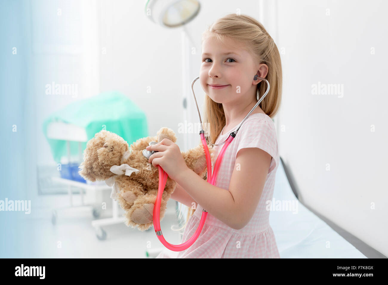Porträt lächelndes Mädchen mit Stethoskop auf Teddybär im Untersuchungsraum Stockfoto