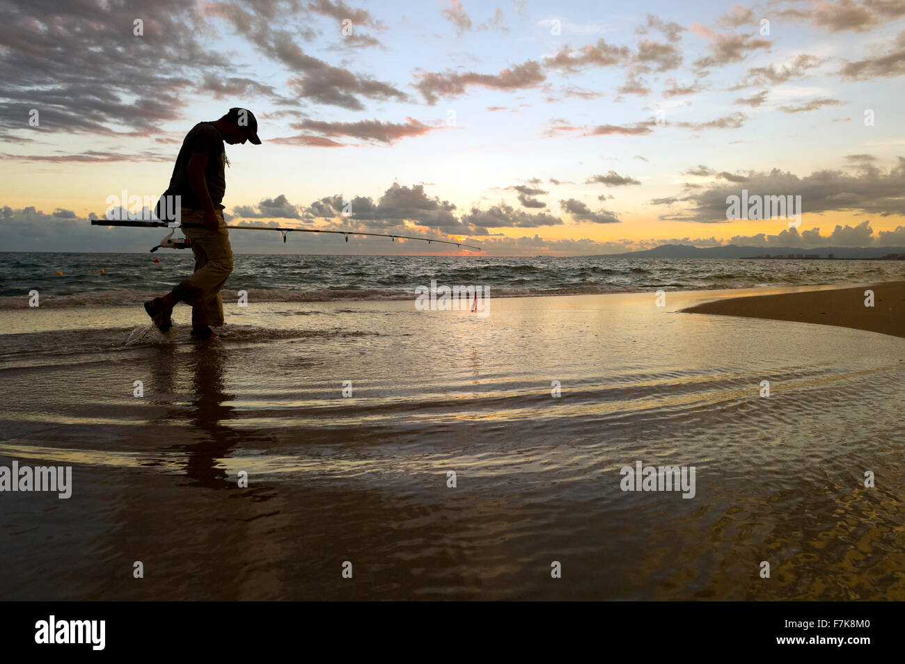 Fischer-Strand ist ein Fischer am Strand entlang spazieren, bei Sonnenaufgang Silhouette gegen den Wolkengebilde Himmel und steigende frühen Mo Stockfoto
