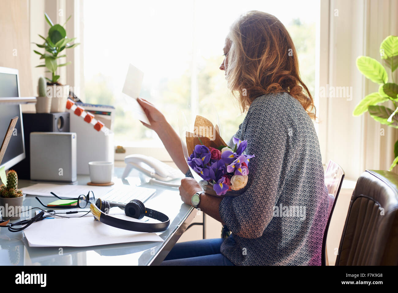 Frau blumeblumenstrauß empfangen und lesen Karte im home-office Stockfoto