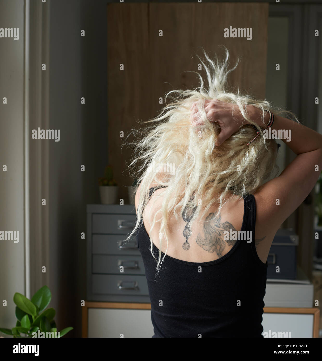 Junge Frau mit Händen im Haar rücken Tätowierungen enthüllt Stockfoto