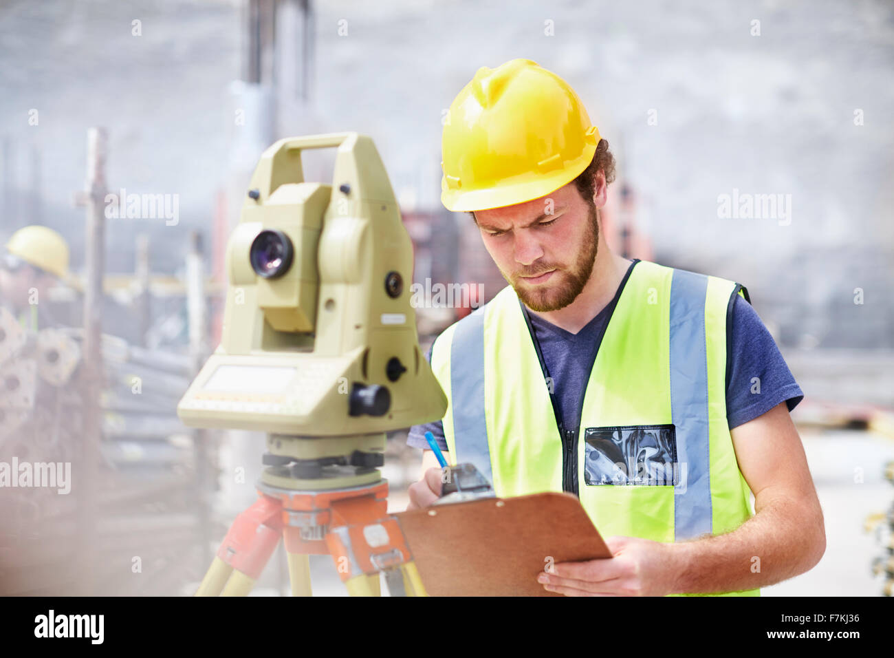 Ingenieur mit Zwischenablage hinter Theodolit auf Baustelle Stockfoto