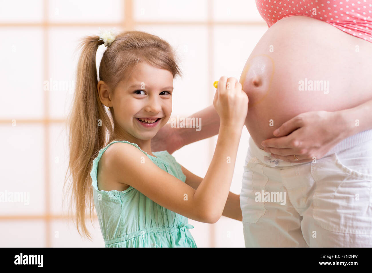 Niedliche kleine Mädchen malt auf den Bauch der schwangeren Mutter Stockfoto