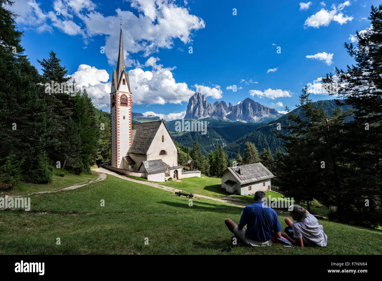 Italien, Dolomiten, Kirche des Heiligen Jakob in der Nähe von St. Ulrich mit zwei Wanderer ruht, Langkofel und Plattkofels im Hintergrund Stockfoto