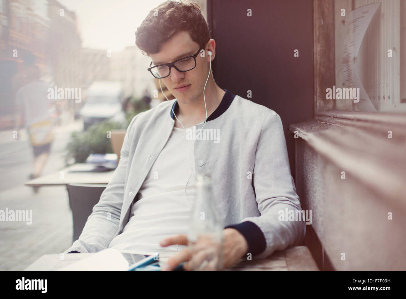 Junger Mann mit Brille und Kopfhörer mit digital-Tablette am Straßencafé Stockfoto