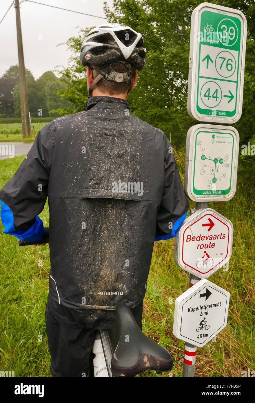 Flandern, Belgien - Radfahrer mit Schlamm am Rücken, am Radweg mit cycling Route Zeichen. Stockfoto