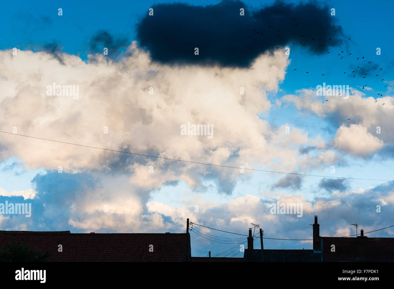 Ein stürmischer, bewölkten Himmel bei Sonnenuntergang in Norfolk mit der Hausdächer als Silhouetten. Stockfoto