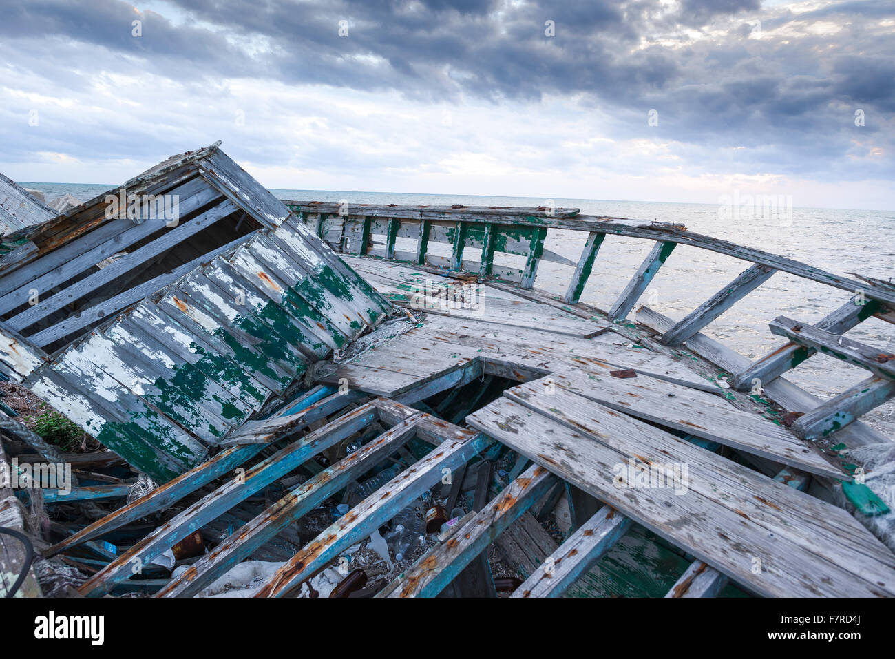 Verlassenes Flüchtlingsboot, Blick auf ein verlassenes Flüchtlingsboot, das dem Verfall überlassen wurde, neben der Meeresmauer in Marsala, Sizilien. Stockfoto
