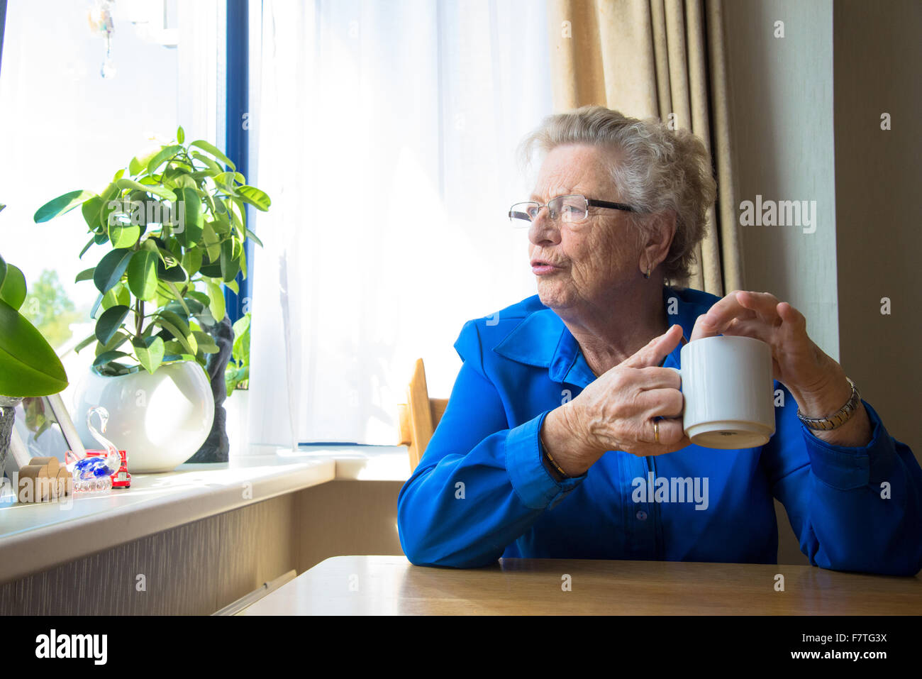 Großmutter, Kaffee trinken und suchen vor ihrem Fenster im Haus für ältere Menschen Stockfoto