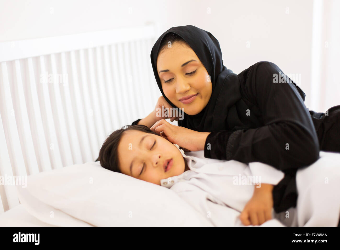 wunderschöne muslimische Mutter, die gerade ihren Sohn im Bett schlafen Stockfoto