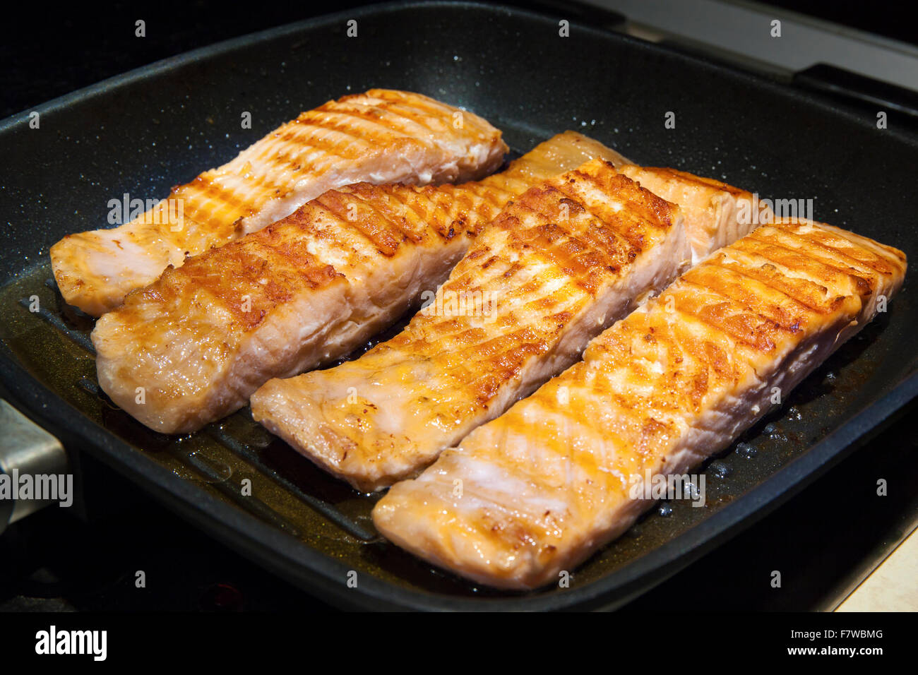 Stücke von einem Fisch Lachs in heiße Pfanne auf Herd kochen. Das Fleisch ist mit einer goldenen Braten Kruste Stockfoto