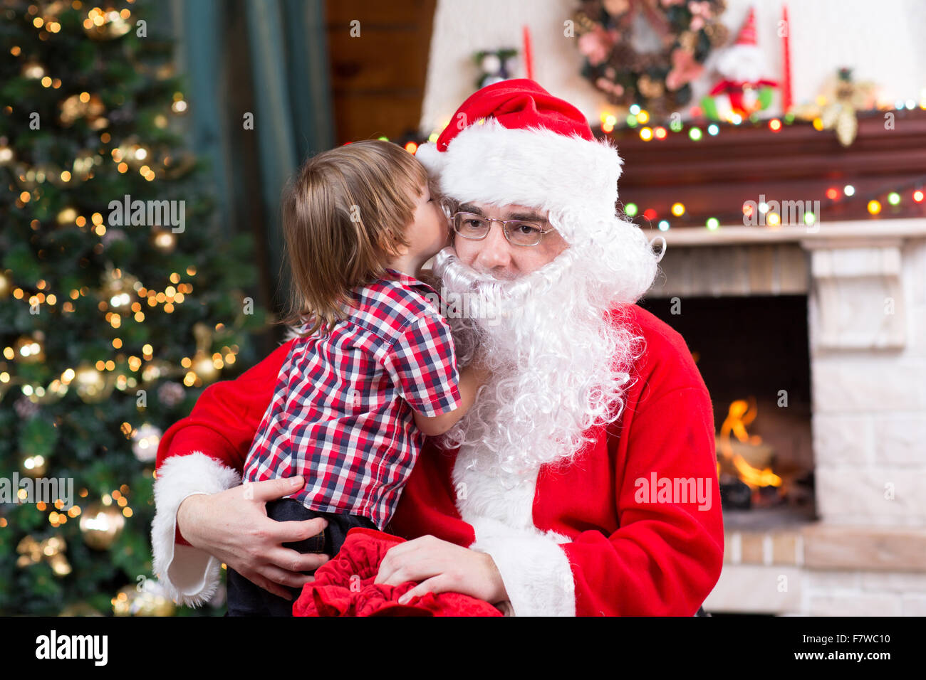 Santa Claus und Kind junge. Kind erzählt seinem Weihnachtswunsch in Santa Claus in der Nähe der Weihnachtsbaum gegenüber Kamin Stockfoto