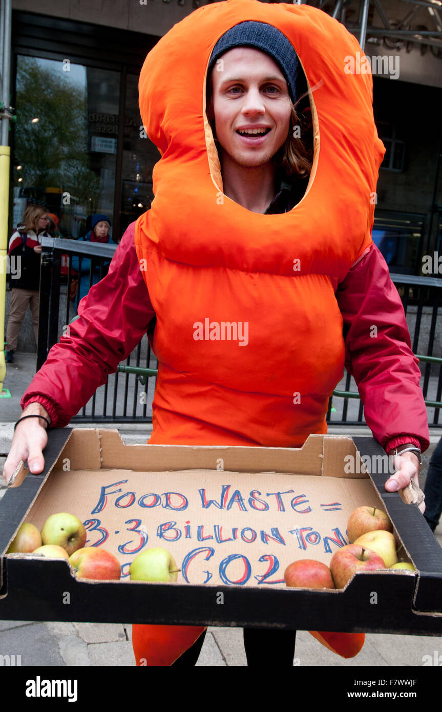 März bis Nachfrage Maßnahmen zur Bekämpfung des Klimawandels. Ein Mann gekleidet wie eine Karotte Äpfel gibt, die Frage von Lebensmittelabfällen markieren Stockfoto