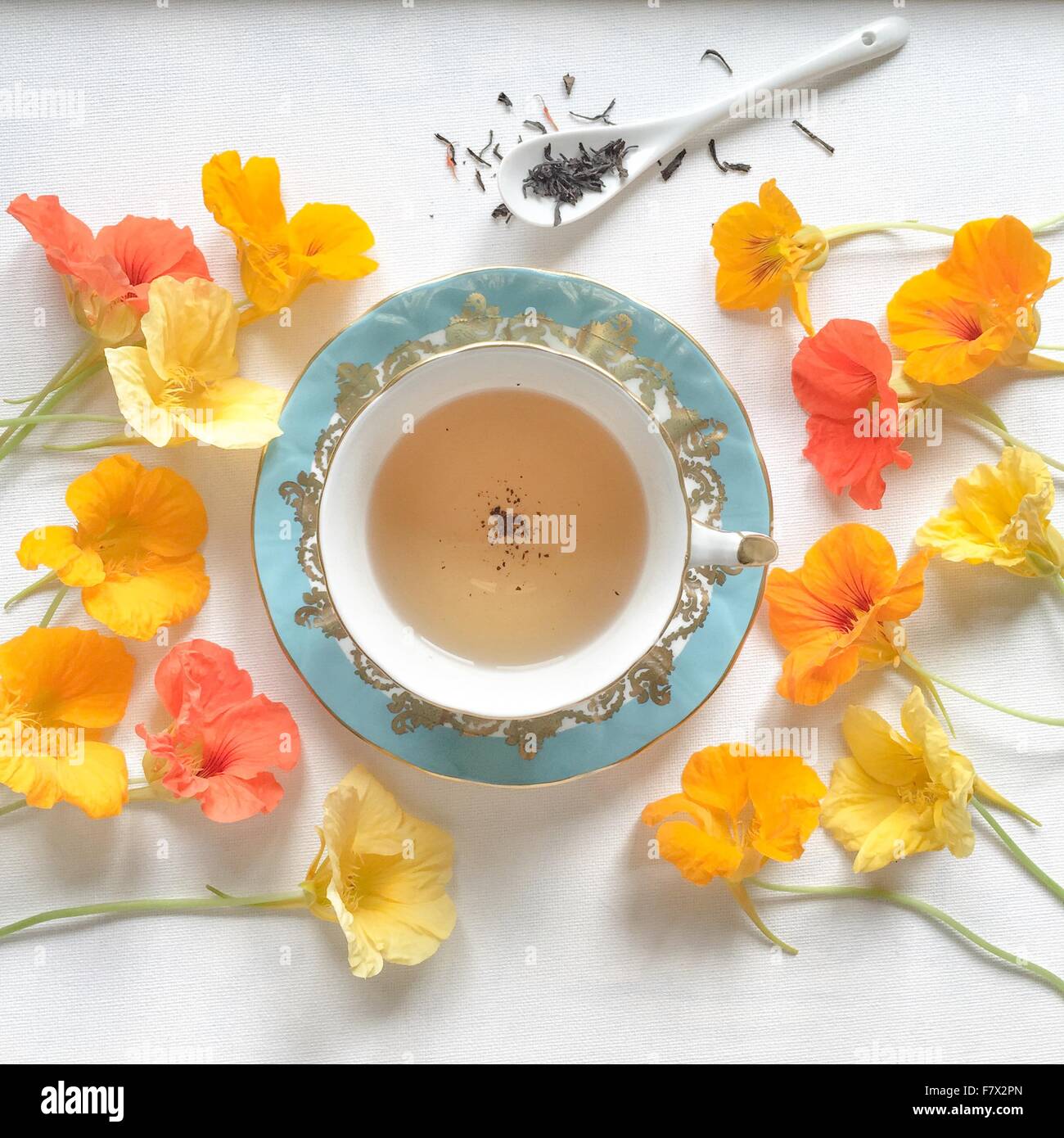 Tasse Tee und ein Löffel Teeblätter umgeben von Kapuzinerkresse Stockfoto