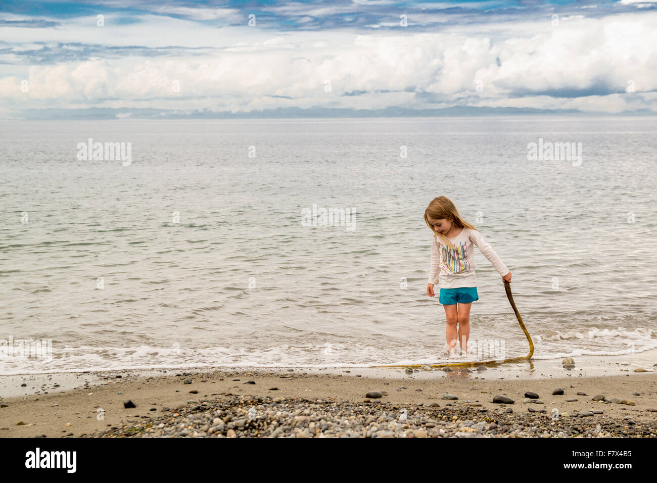 Mädchen stehen am Strand hält einen Stock Stockfoto