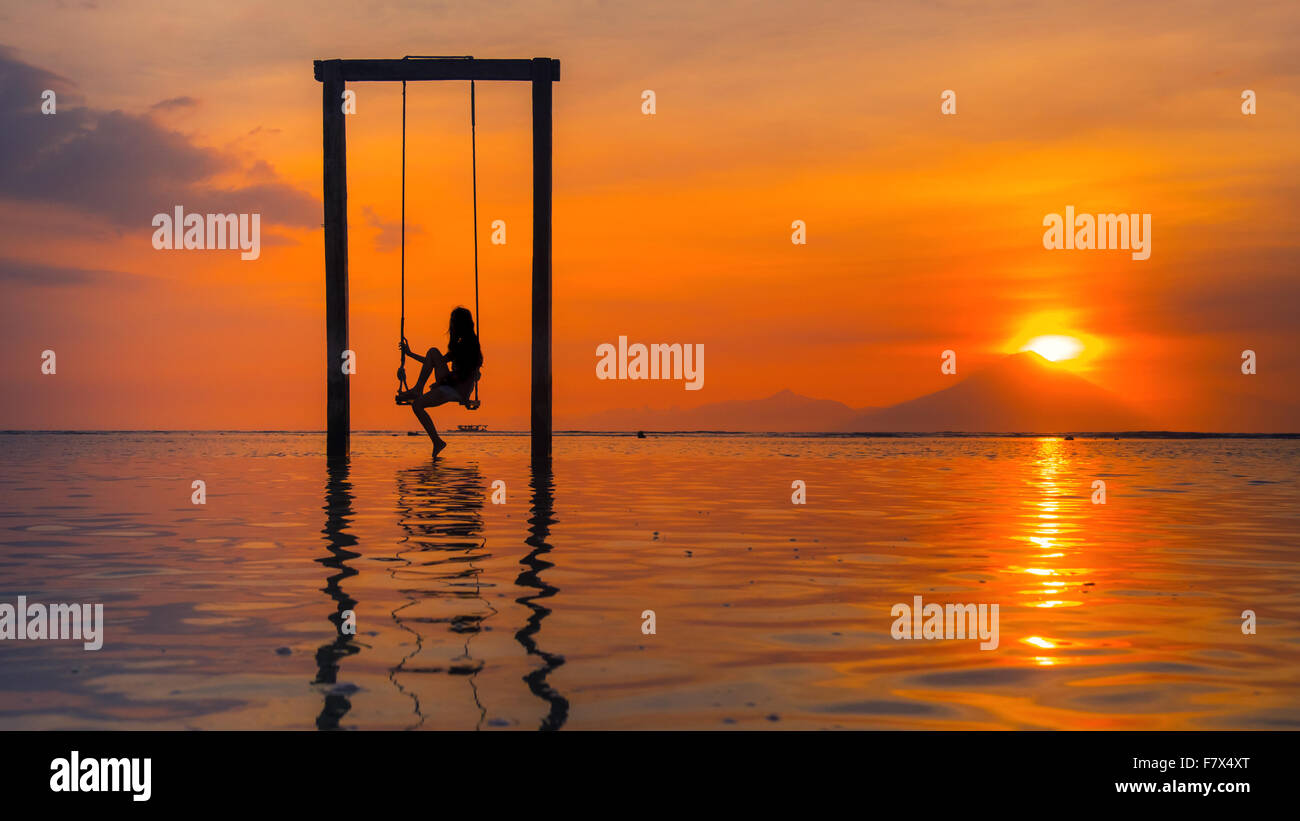 Silhouette einer Frau sitzt auf einer Schaukel im Meer bei Sonnenuntergang, Indonesien Stockfoto