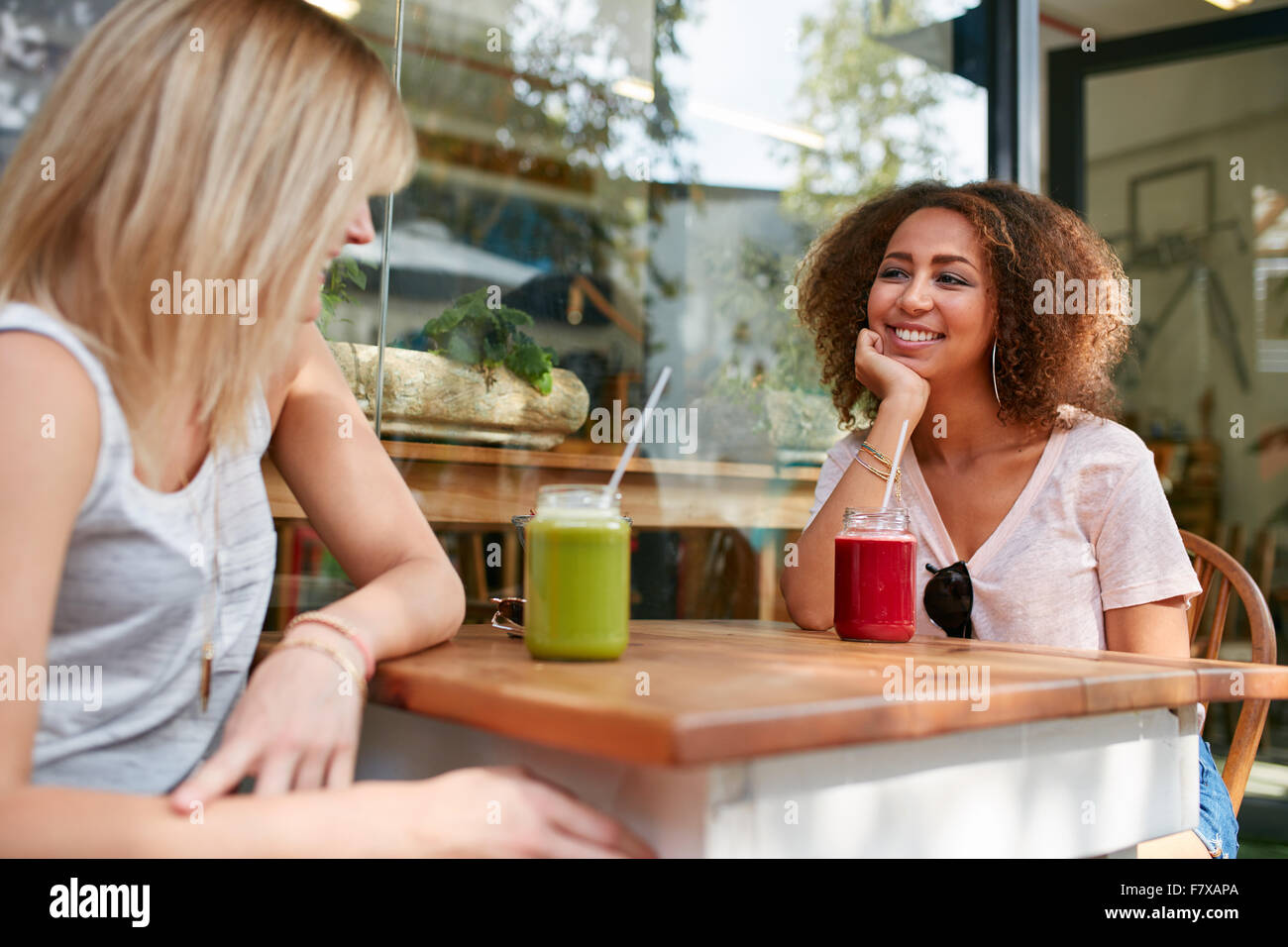 Bild der jungen afrikanischen Mädchen sitzt mit ihrer Freundin im Café im Freien. Zwei junge Frauen treffen im Straßencafé mit alkoholfreien Cocktails. Stockfoto